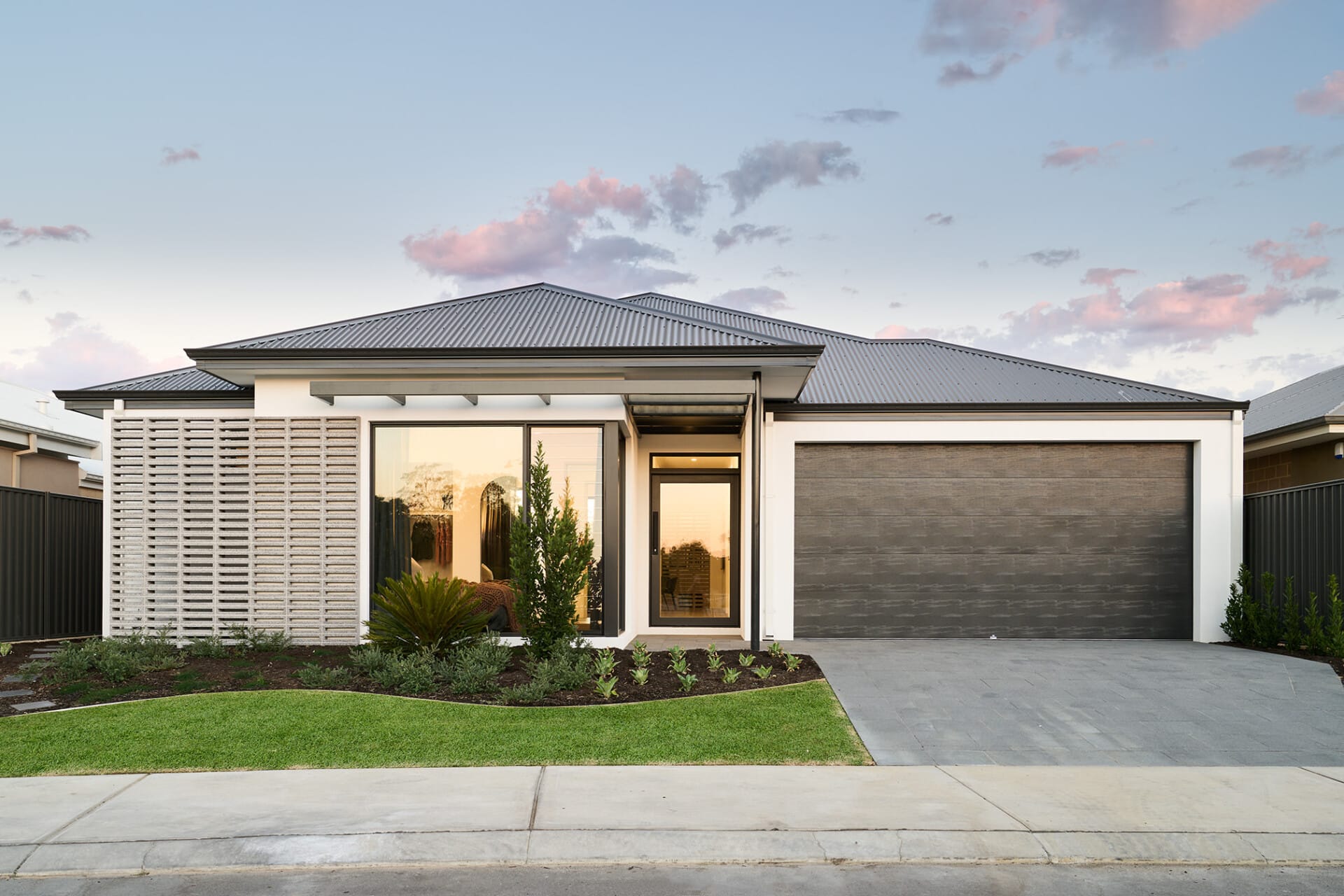 Modern single-story house with white facade, large windows, sleek roof, and landscaped front yard.